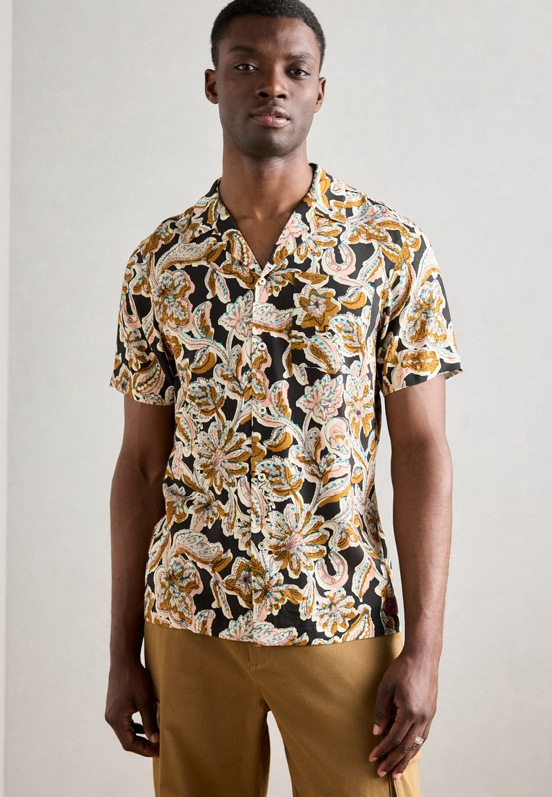 Μπλουζάκι κοντού μανικιού σε μαύρο χρώμα με περίπλοκο λουλουδάτο σχέδιο σε χρυσό, ροζ και μπλε. Ελαφρύ ύφασμα με χαλαρή εφαρμογή και κλείσιμο με κουμπί.