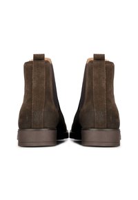 Botas de tobillo de ante marrón oscuro con paneles elásticos en los lados y un acabado texturizado. Suelas de goma planas y detalles cosidos a lo largo de las costuras.