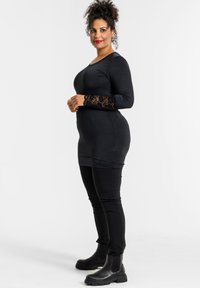 Sort langærmet kjole med blonder på ærmerne, parret med sorte leggings og ankelstøvler. Glat tekstur og tætsiddende pasform.