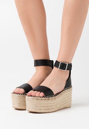 Zwarte leren platform sandalen met een geweven jute zool, voorzien van een enkelsluiting met een zilveren gesp en brede tebanden.
