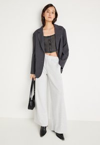 Γκρίζα σαλοπέτα πάνω από μαύρο κοντό τοπ με ριγωτή υφή, συνδυασμένο με γκρίζα παντελόνια φαρδιάς γραμμής και μαύρες μυτερές γόβες. Κρατάει μια μαύρη τσάντα.