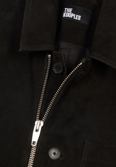 Czarna zamszowa kurtka z częściowo zasuniętym srebrnym zamkiem błyskawicznym, czarne guziki z wytłoczonym napisem "The Kooples" oraz kołnierz.