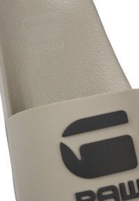 Sandale à enfiler à bout fermé en matière synthétique beige avec une finition texturée. Dispose d'un logo noir et d'une large sangle.