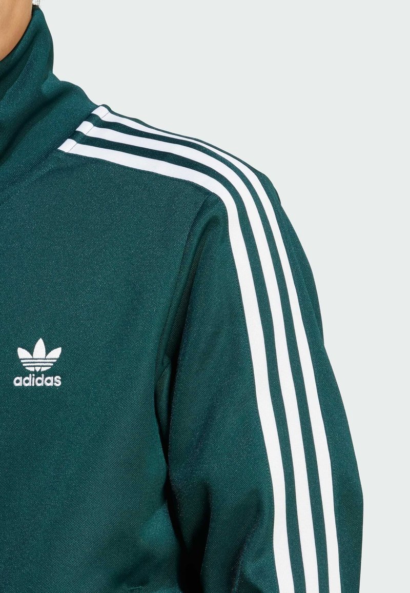 Tamnozeleni Adidas trenirku s visokim ovratnikom, bijelim trostrukim trakama na ramenima i bijelim logotipom na prsima.