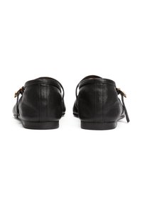 Mocasines de cuero negro con un tacón bajo, que presentan un detalle de lazo lateral y una textura suave. El diseño incluye costuras a lo largo de los bordes.