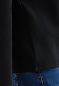 Schwarzes Langarmshirt mit glatter Textur und figurbetontem Schnitt, mit einer dezenten Nahtdetails am Saum, kombiniert mit blauer Denim.