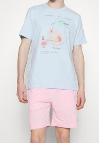 T-shirt en coton bleu clair avec un texte graphique et un logo Jumpman, associé à un short rose. Les deux vêtements ont une coupe décontractée et une texture lisse.