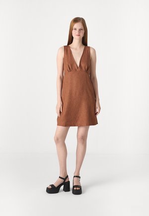Robe sans manches marron avec un décolleté en V profond et une taille froncée. Portée avec des sandales à plateforme noires, mettant en valeur une texture lisse et une forme élégante.
