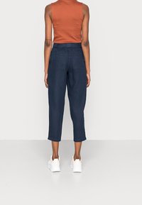 Pantalones recortados azul marino de mezclilla, con una cintura alta, bolsillos laterales y puños enrollados, combinados con una camiseta sin mangas ajustada de color óxido.