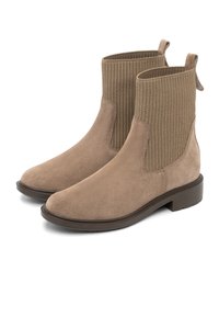 Smėlio spalvos nubuko apavo kulkšninių batai su raižytais elastiniais įdėklais, traukimo kilpa ir žema blokine pakulne. Lygaus paviršiaus tekstūra su švariu, elegantišku dizainu.