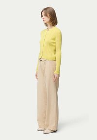 Gul ribbad stickad cardigan med långa ärmar, i kombination med beige vida byxor och mönstrade slipskor. Enkla och moderna linjer.