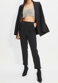 Černý skvěle padnoucí blazer přes stříbrný top s flitry, spárovaný s černými tapered kalhotami a černými kotníkovými botami, vytvářející štíhlou siluetu.