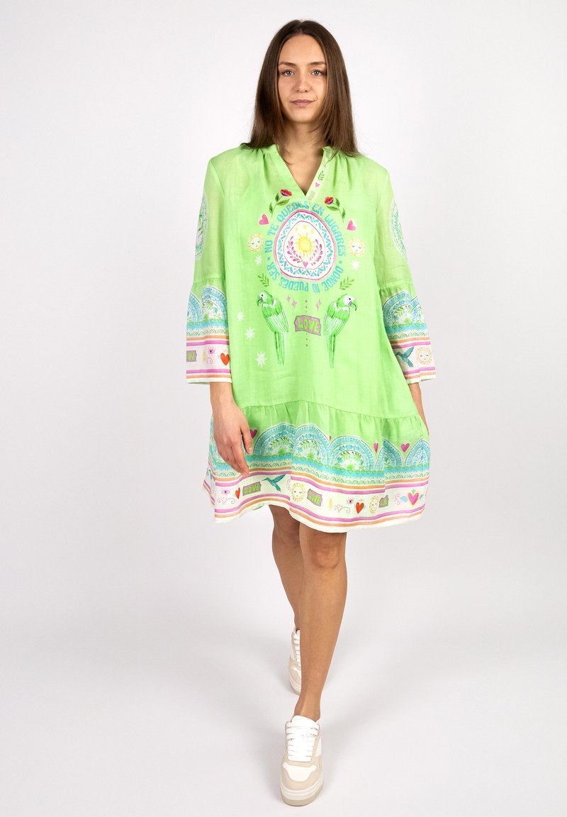 Hellgrünes, knielanges Kleid mit weitem Ausschnitt, das bunte Drucke von Papageien und Mandalas sowie dekorative Ränder mit Herzen zeigt.