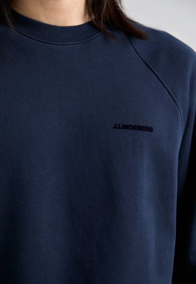 Sudadera azul marino hecha de suave algodón, con cuello redondo y mangas raglán. Un sutil logo negro está ubicado en el pecho.