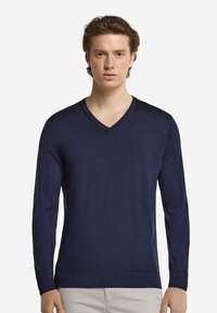 Marinblå långärmad v-neck-tröja gjord av ett mjukt, lätt material med ribbade manschetter och nederkant. Enkel, klassisk design.