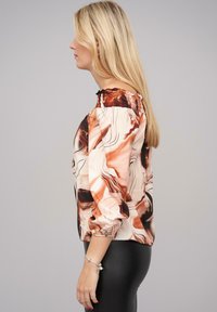 Blusa a maniche lunghe in tessuto setoso con un motivo marmorizzato in toni terrosi di beige, marrone e nero. Collo e polsini elasticizzati.