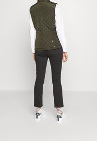 Olivgrön kviltad väst med en figurnära design, hög krage, tryckknappdetaljer, i kombination med svarta byxor och vita sneakers med gröna accenter.