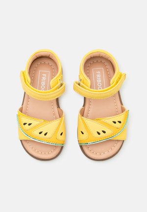 Gelbe Sandalen mit einem Wassermelonenmotiv, ausgestattet mit Überkreuzriemen und schwarzen Samenakzenten. Hergestellt aus synthetischem Material mit einer strukturierten Sohle.