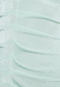 Tissu vert menthe clair avec des fronces horizontales, présentant une texture lisse et une finition légèrement brillante, créant des détails en vagues structurés.