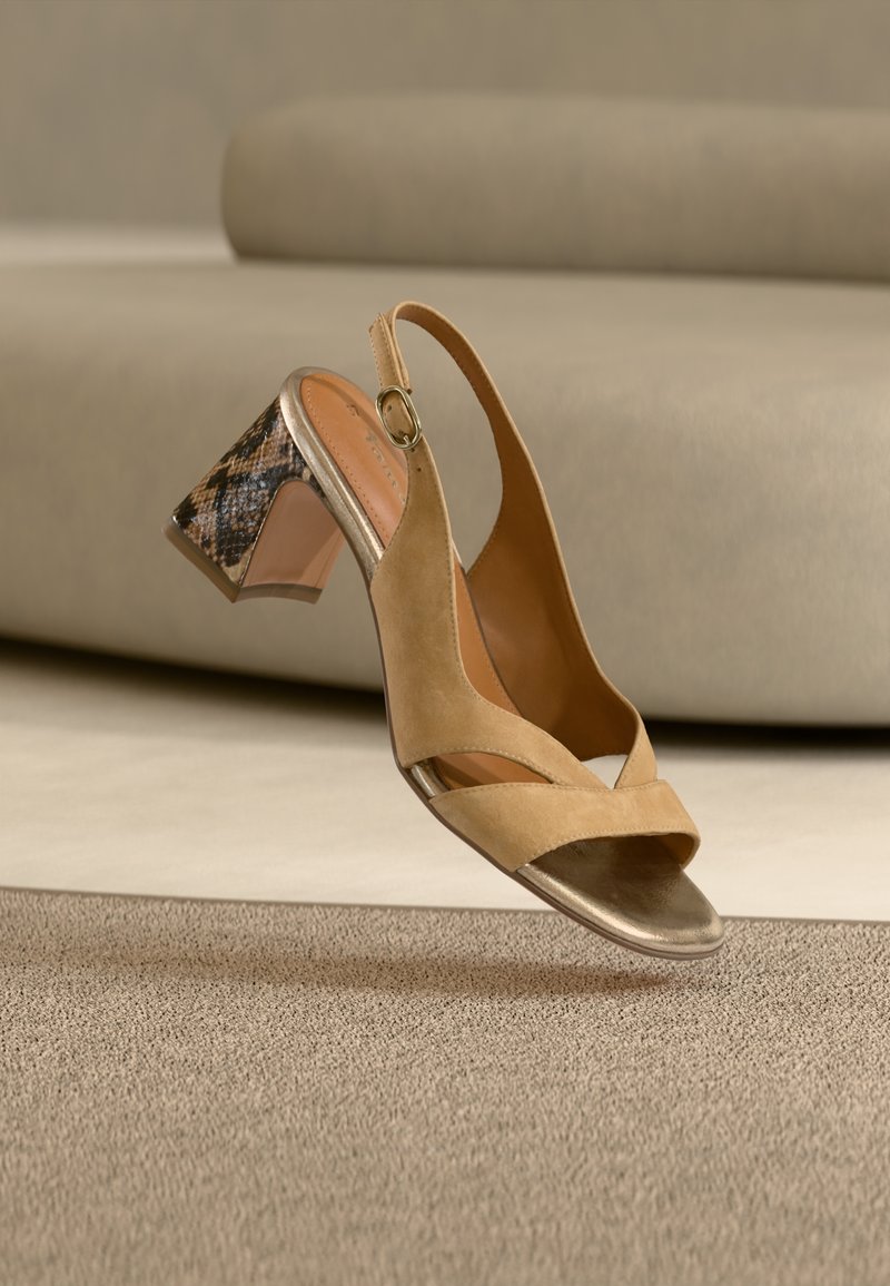 Μπεζ σατέν πέδιλο με ανοιχτά δάχτυλα και χοντρό τακούνι με καφέ μοτίβο φιδιού, τοποθετημένο σε μπεζ χαλί.