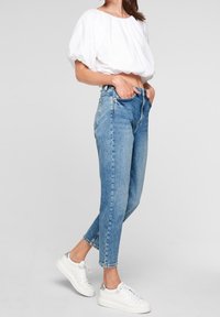Light blue high-waisted jeans with a slim fit, featuring classic five-pocket design and cuffed hems, paired with a white cropped blouse.