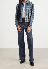 Kariertes Cropped-Jacket in Blau und Grün mit metallischen Knöpfen, kombiniert mit hochtaillierten dunklen Denim-Hosen und schwarzen, hochhackigen Stiefeletten.