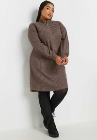 Brun ribbad klänning med hög krage och dragkedja, med långa puffärmar och avslappnad passform, kombinerad med svarta snörstövlar.