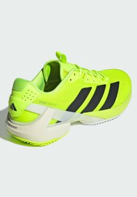 Chaussure de sport jaune vif avec des rayures noires, présentant un dessus en mesh texturé, un contre-pied de soutien et un design de semelle légère.