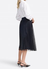 Schwarzer Tüll-Midirock mit Falten und Polka-Dot-Akzenten, kombiniert mit einem weißen Hemd mit Knöpfen. Verfügt über einen hohen Bund und eine geschichtete Textur.