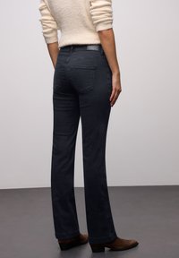 Vaqueros de mezclilla oscura acampanados con cintura alta, que cuentan con dos bolsillos traseros y detalles sutiles de costura. Combinados con un suéter ligero y de textura.