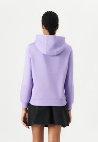 Sudadera con capucha lavanda hecha de material suave, con un bolsillo delantero tipo canguro y puños acanalados. Combinada con una falda negra.