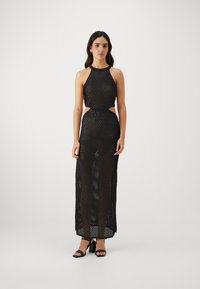 Robe en maille noire avec col halter, taille découpée et longueur de sol. Tissu texturé et apparence transparente avec un matériel minimal.