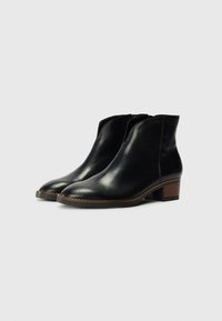 Bottines en cuir noir avec un bout rond, un petit talon carré et des panneaux élastiques sur les côtés pour faciliter l'enfilage. Texture lisse et design minimaliste.