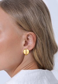 Goldene, runde Steckerohrringe mit einem horizontalen Linienmuster. Glatte, metallische Oberfläche und polierte Oberfläche, getragen am Ohr eines Modells.