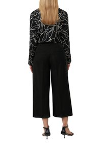 Zwarte wijde broek gecombineerd met een zwart-wit gestreepte blouse met lange mouwen, voorzien van een bloemenpatroon en knoopmanchetten.