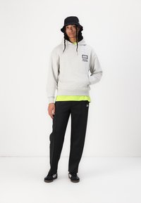 Grå fleece hettegenser med frontlomme, grønn lagdelt skjorte under, svarte bukser, svart bøttehatt og svarte sneakers med hvite striper.
