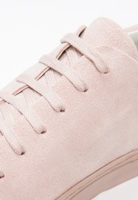 Baskets en daim rose clair avec des lacets assortis bien serrés, mettant en avant la texture douce et un design épuré et minimal.