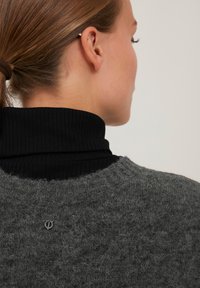 Hall grey kudum, millel on tekstuurilised detailid, must ribitud kõrge kaelusega särk all ja väike logo aktsent taga.