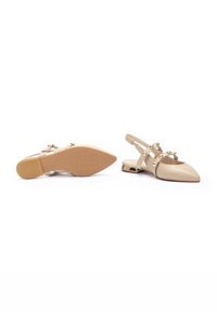Scarpe slingback beige con punta affilata e tacco piatto. Presentano delle cinghie decorative con decorazioni rotonde. Finitura in pelle liscia.