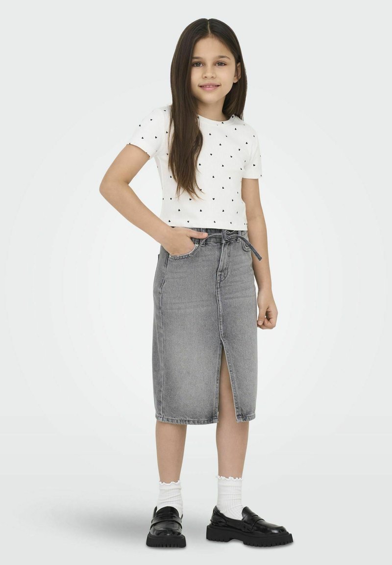 Baltas trumpas rankovės marškinėliai su juodais širdelių raštais, derinami su pilka džinsine midi sijonu su priekinėje pusėje iškirpimu ir virvute liemenyje. Juodi batai.