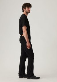 Μαύρο μπλουζάκι και μαύρο τζιν παντελόνι που φοριέται από ανδρική φιγούρα, πλαϊνή όψη. Το μπλουζάκι είναι με κοντά μανίκια, το τζιν έχει κλασική ίσια γραμμή και εμφανείς τσέπες.