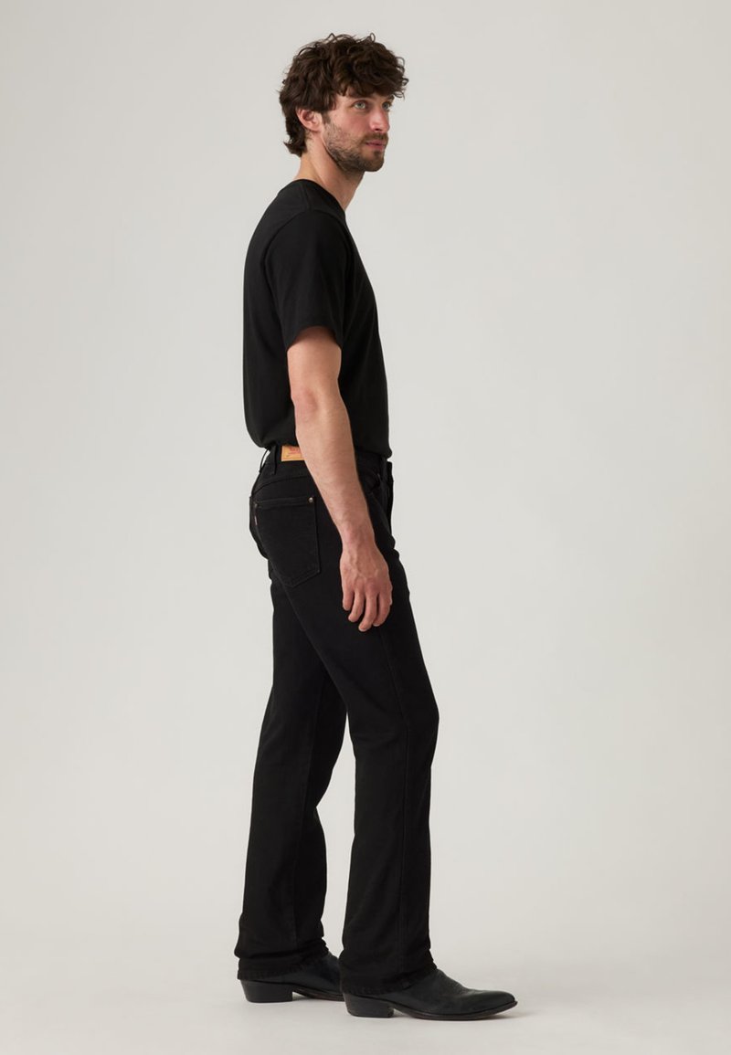 Maglietta nera e jeans in denim nero indossati da una figura maschile, vista laterale. La maglietta è a maniche corte, i jeans hanno una vestibilità classica dritta e tasche visibili.