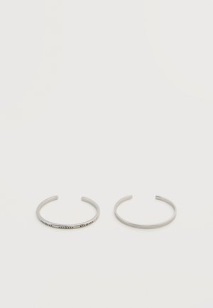 Δύο λεπτές ασημένιες βραχιόλια για μανσέτες, το ένα απλό και το άλλο χαραγμένο με Μπράιγ, σε ουδέτερο φόντο.