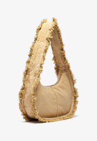 Beige stoffveske med avrundet form og frynset kant. Har en glidelåslomme og en bred skulderrem for enkel bæring.