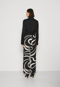 Zwarte blouse met lange mouwen, gecombineerd met een patroon van brede broek met witte abstracte draaikolken, vergezeld van hoge hakken.