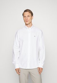 Camicia bianca in cotone. Presenta un colletto classico, maniche lunghe e un piccolo logo ricamato sul petto. Texture liscia.