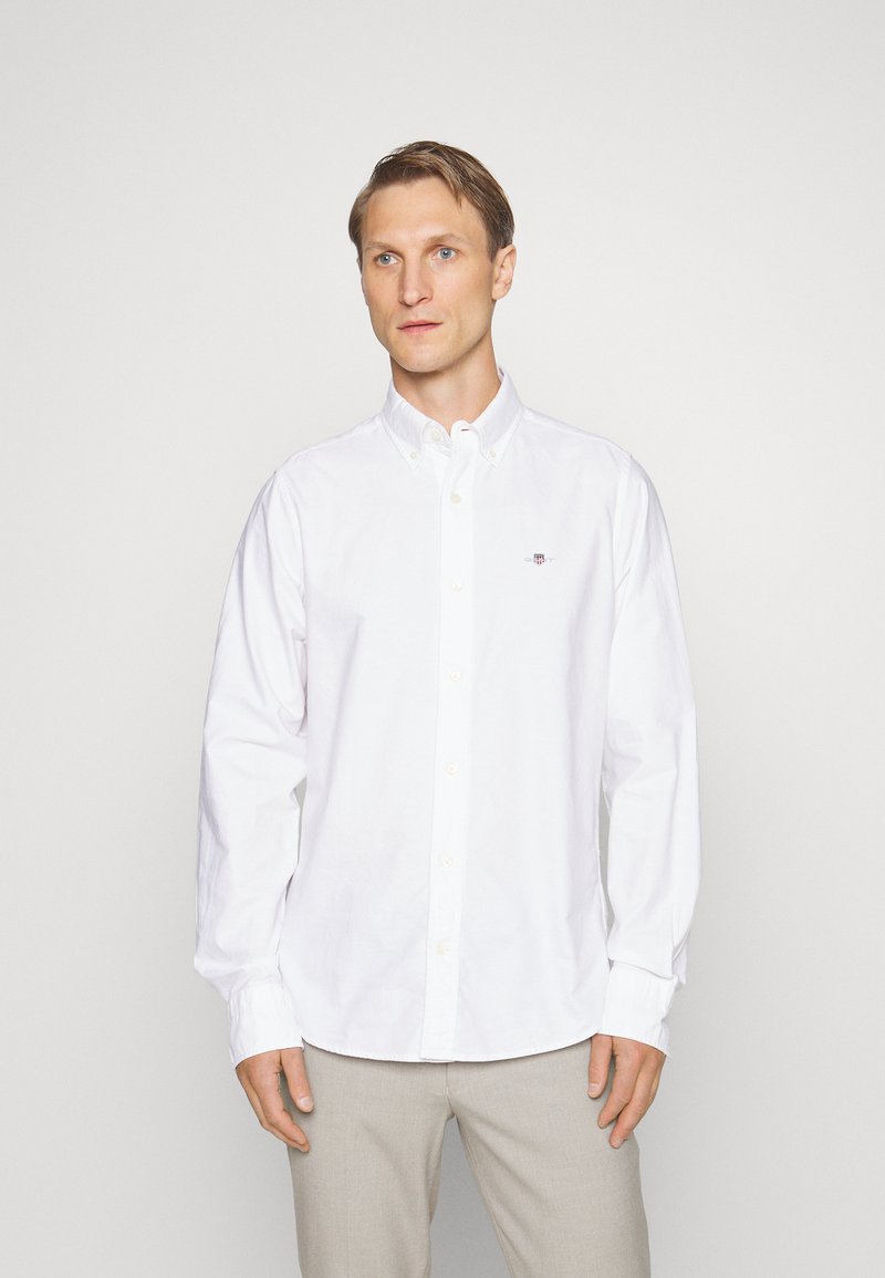 Camicia bianca in cotone. Presenta un colletto classico, maniche lunghe e un piccolo logo ricamato sul petto. Texture liscia.