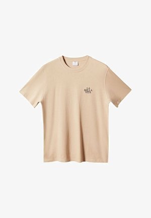 Beżowy T-shirt z krótkim rękawem i okrągłym dekoltem, z małym czarnym napisem „LA BELLA VITA” na górnej lewej części klatki piersiowej.