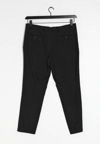 Černé kalhoty slim fit, s kapsami na zadní straně, poutky na opasek a hladkým povrchem. Visí na černém plastovém ramínku.