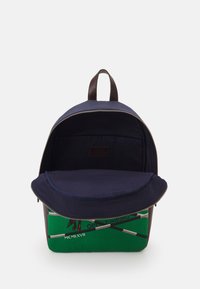 Greene canvas ryggsäck med marinblå textilinteriör och bruna läderdetaljer. Utrustad med dragkedjestängning och en framficka med lock.